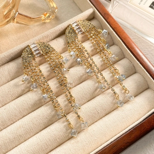 Macro shot of long gold tassel bridal earrings with zircon stones on beige velvet