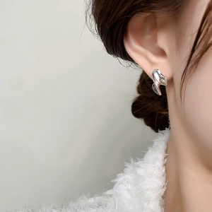 Close-up of irregular liquid-style silver metal stud earrings on female ear