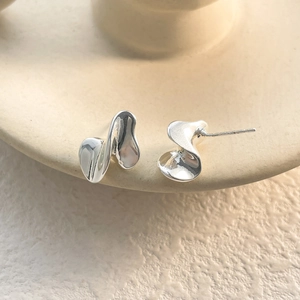 Detailed view of polished irregular molten silver earrings on elegant ceramic display