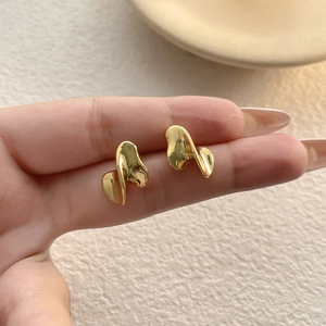 Macro view of gold-plated irregular fluid earrings held in hand for scale detail