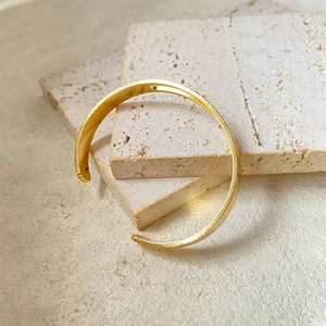 Close-up of a minimalist golden C-shaped open cuff bracelet on beige marble stone