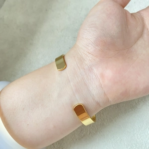 Close-up of a minimalist gold-plated open cuff bangle featuring a smooth mirror finish