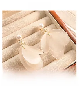 Detailed view of elegant white shell tassel earrings with pearls on beige velvet surface