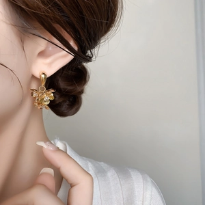Détail d'une boucle d'oreille fleur 3D dorée avec zircons portée par un mannequin