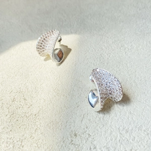 Macro detail of silver twisted heart earrings with pavé zircons and polished finish