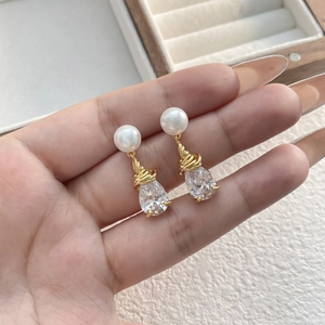 Détail de boucles d'oreilles perles avec zircon goutte et design en fil d'or torsadé