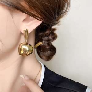 Close-up of a polished gold irregular bean-shaped droplet earring on a model