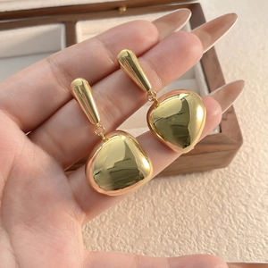 Polished 18K gold-plated heart-shaped tassel earrings on a wooden jewelry box display