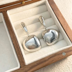 Detailed view of polished silver tassel earrings with a glossy mirror finish on white velvet
