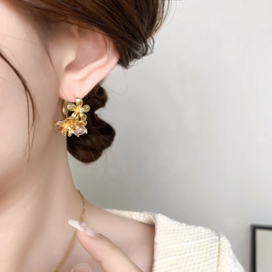 Détail de boucles d'oreilles fleurs dorées avec zircon porté sur le lobe d'oreille