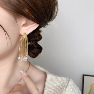 Detailed view of long gold tassel earrings with shimmering zircon bead chains on model