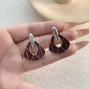 Detail of vintage asymmetric red enamel earrings with silver geometric patterns held in hand