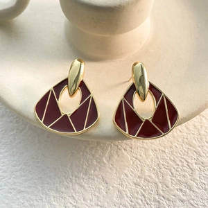 Detail of vintage gold earrings with deep red enamel on a cream ceramic holder