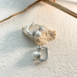 Detailed shot of vintage French pearl earrings with silver clasp on natural stone background