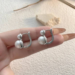 Close-up of elegant double pearl earrings in silver finish being held by hand