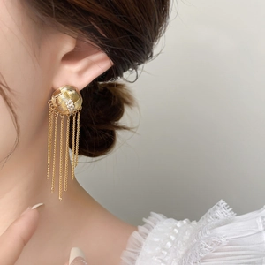 Gros plan de boucles d'oreilles dorées à pompons avec base soleil et chaînes sur mannequin