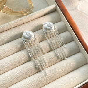 Détail de boucles d'oreilles à pompons argentés avec boules tressées sur velours beige