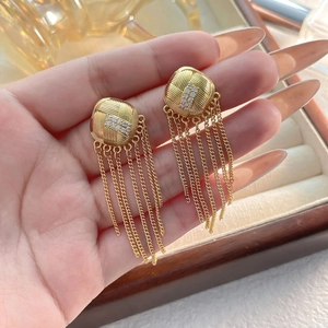 Détail macro de boucles d'oreilles dorées avec carrés tressés et rangées de zircons brillants