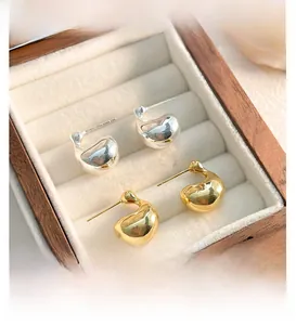 Macro detail of polished gold and silver bean-shaped stud earrings in a wooden jewelry box