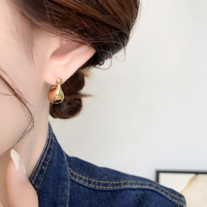 Close-up of minimalist golden teardrop stud earrings worn on ear with mirror finish
