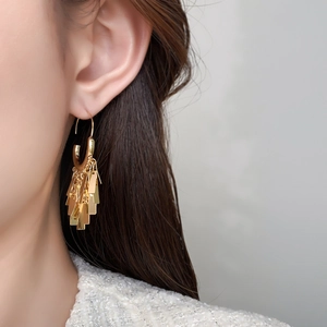 Close-up of golden geometric tassel earrings with polished metallic fringe on model