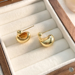 Close-up of golden irregular chunky teardrop earrings in a wooden jewelry box