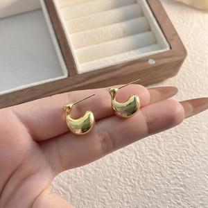 Minimalist gold curved earrings with a high-polished finish held in hand near a box