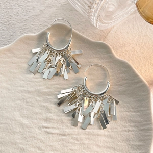 Detailed view of silver hoop earrings with cascading rectangular tassel charms on ceramic plate