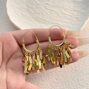 Golden hoop earrings with long metallic fringe tassels held over a white ceramic dish