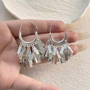 Detailed close-up of silver rectangle tassel earrings held by hand over a white plate