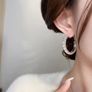 Close-up of a model wearing large silver hoop earrings paved with sparkling zircon stones
