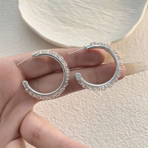 Macro shot of silver C-shaped hoop earrings with full pave cubic zirconia crystals