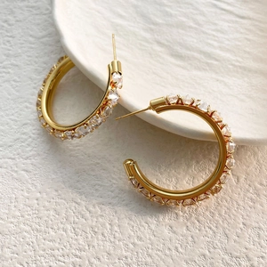 Macro view of gold-plated C-shaped earrings with micro-paved white zircon stones