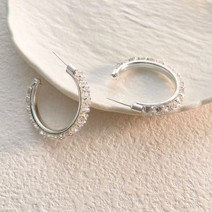 Macro shot of silver C-hoop earrings with sparkling pavé crystals on a ceramic tray