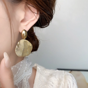 Detail view of gold metal drop earrings with textured circular pendants on model