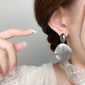 Detail of silver drop earrings with smooth oval top and textured round sunburst pendant