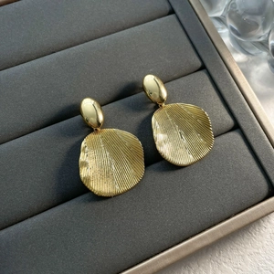 Detailed view of gold earrings with polished studs and textured fan-shaped pendants