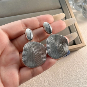 Detail showing oversized silver irregular earrings with textured radial wavy patterns