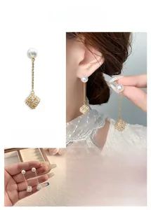 Dettaglio di orecchini lunghi con perle e pendente a cubo in zircone oro e argento
