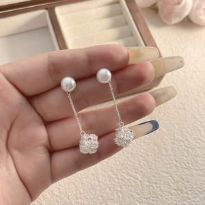 Dettaglio di orecchini a perla lunga con catena d'argento e ciondolo a sfera di cristallo