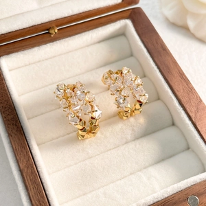 Détail de boucles d'oreilles C dorées avec zircons sertis dans un écrin