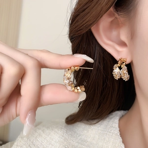 Boucles d'oreilles C dorées étincelantes avec zircons portées sur l'oreille
