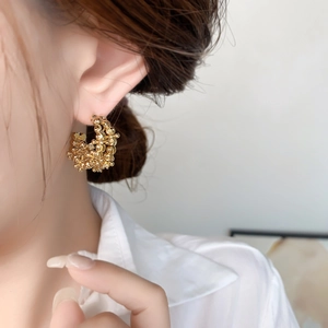 Detailed close-up of golden C-shaped hoop earrings with textured beaded surface on model