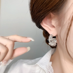 Detail of silver C-shaped earring with textured bead clusters worn by a model