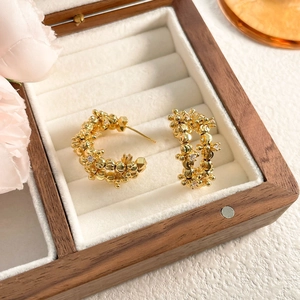 Detail of gold C-shaped earrings with beaded texture and zircon in a wooden box