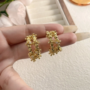 Close-up of golden C-shaped earrings with textured surface and sparkling zircon details