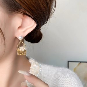 Close-up of elegant gold woven basket earrings with white pearls on a female model
