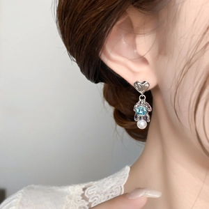 Close-up of heart-shaped silver earrings with blue gemstone and white pearl on model