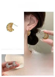 Detailed view of textured C-shaped gold and silver earrings with a liquid metal lava effect