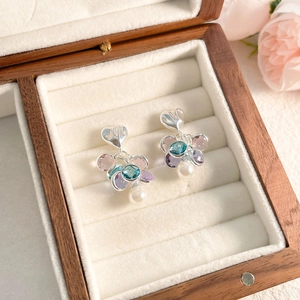 Detailed shot of silver heart earrings with colorful gems and white drop pearls in a box